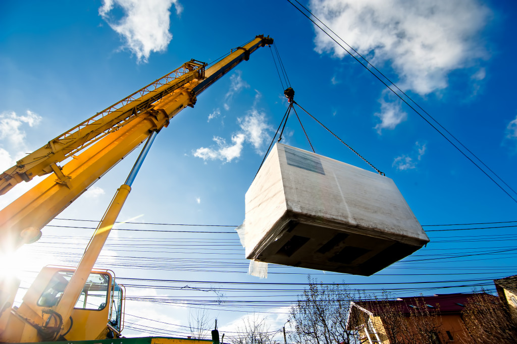 Industrial Crane operating and lifting an electric generator against sunlight and blue sky