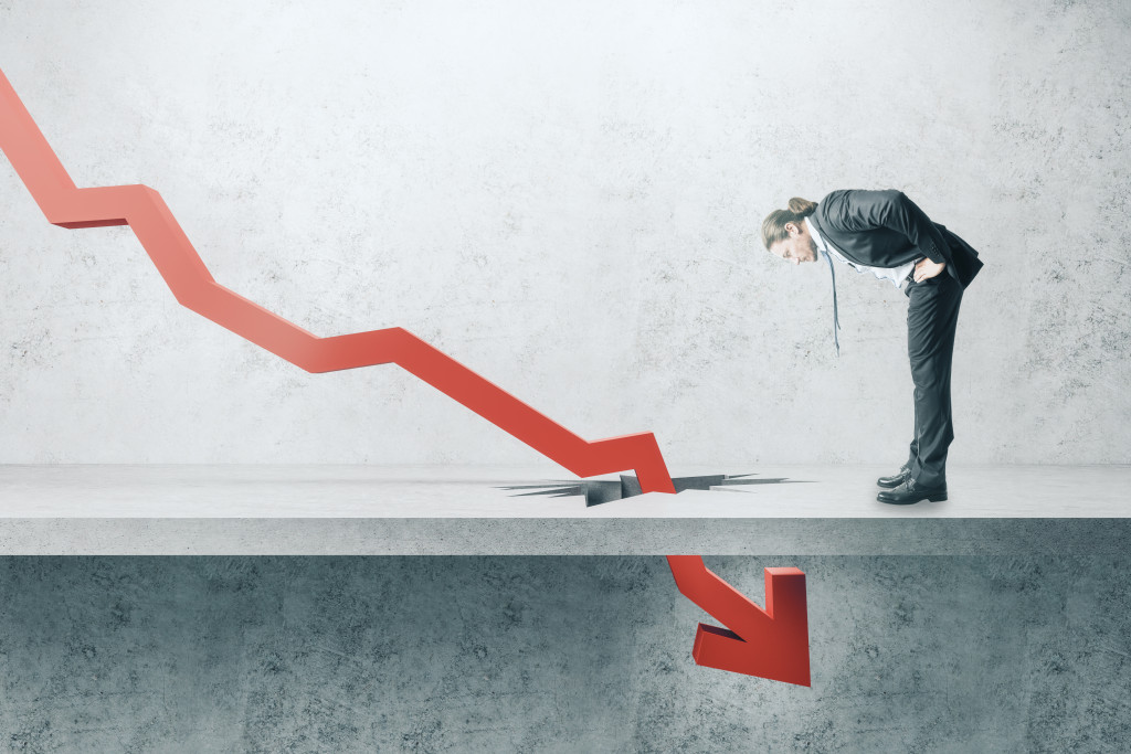 A businessman looking down at a falling red arrow breaking through concrete ground