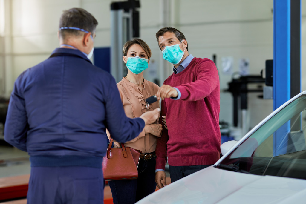 A couple wearing facemasks giving the keys of their car to a mechanic in the shop