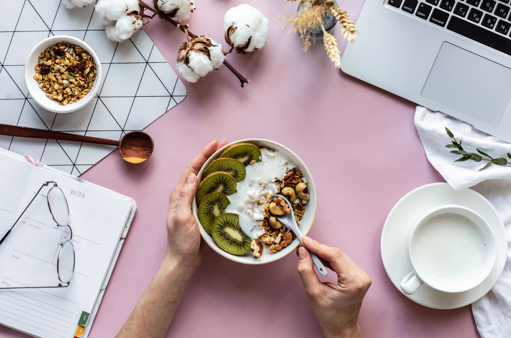 a person eating a bowl of fruits in front of a laptop on a pink table