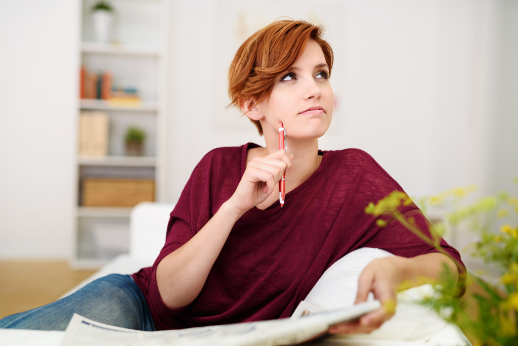 adult woman in the couch answering puzzle in the newspaper