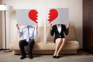 man and woman holding halved cardboard with broken heart in a couch